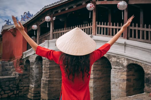 back of woman tourist in a Vietnamese hat Non La at ancient Japanese covered bridge in old town in Hoi An in Vietnam in Asia