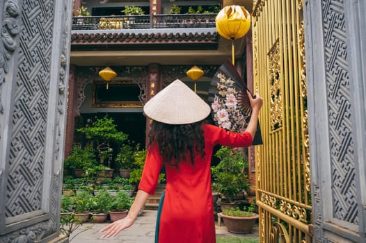 back of a female traveler tourist in a Vietnamese hat at a Buddhist temple in Hoi An in Vietnam in Asia