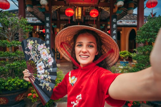 Selfie portrait of a happy young beautiful woman tourist in a Vietnamese hat at a temple in Asia in Vietnam