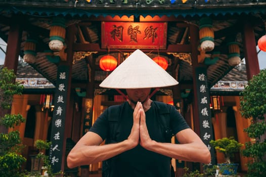 male tourist in Vietnamese Non La hat prays at a temple on a Buddhist pagoda in Vietnam in Asia