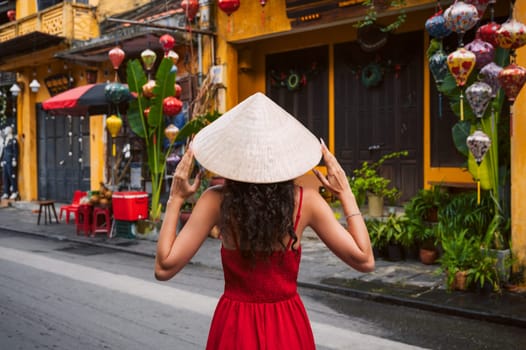 back of asian woman tourist in a traditional Vietnamese hat and red dress on the street in Hoi An city in Vietnam in Asia