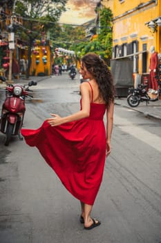 back of a young beautiful female tourist traveler in a red dress on the street in the old town in Hoi An in Vietnam in Asia