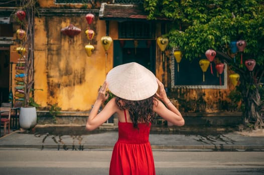 back of a young beautiful asian girl tourist in a traditional Vietnamese hat on street in old town in Hoi An city in Vietnam