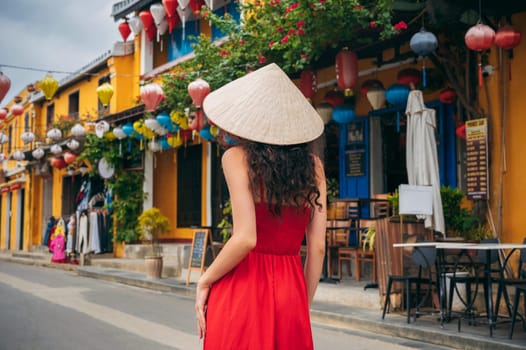 back of asian woman tourist in traditional Vietnamese hat and red dress on street in old town in Hoi An city in Vietnam in Asia