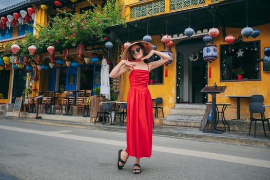 happy young female tourist traveler in traditional Vietnamese hat and red dress on street in Hoi An city in Vietnam in Asia