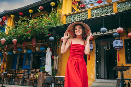 happy beautiful girl tourist in Vietnamese hat and red dress on the street in the old town in Hoi An city in Vietnam in Asia