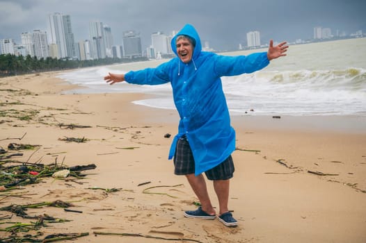 happy man tourist in a raincoat on a dirty beach by the sea after a storm in cloudy weather. The concept of the rainy and monsoon season