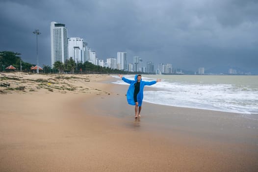 male in a raincoat on beach by sea with waves in cloudy weather with rain. Concept of rainy and monsoon season in Nha Trang in Vietnam