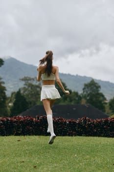 A young woman wearing a white athletic ensemble runs on lush grass, displaying a sense of freedom and energy in a scenic outdoor backdrop, emphasizing fitness and well being