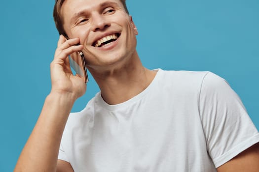 Engaged smiling man enjoying a phone call, relaxed casual style, young adult male with a bright smile, candid moment, vibrant blue studio background, positive communication and social interactions concept
