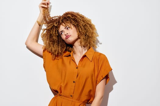 A confident woman with curly hair wearing an orange dress poses against a clean, white backdrop Her playful expression and hair styling emphasize her unique personality and fashion sense, surrounded