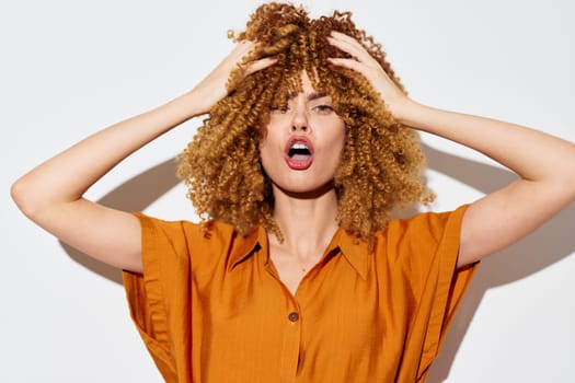 This vibrant image features a woman with voluminous curly hair, passionately expressing herself She wears an orange shirt against a clean white background, creating a dynamic contrast