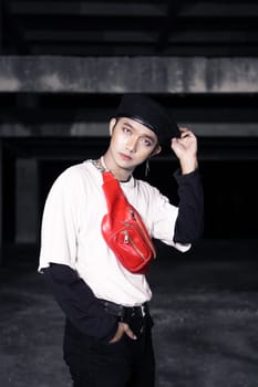 an Asian man in a white shirt wearing a red bag and a black hat in an old building at night