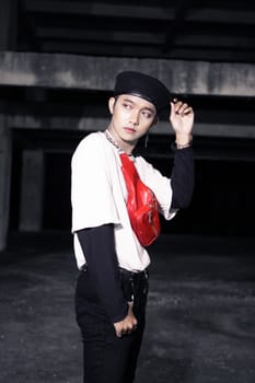 an Asian man in a white shirt wearing a red bag and a black hat in an old building at night