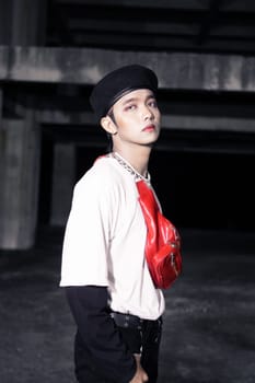 an Asian man in a white shirt wearing a red bag and a black hat in an old building at night