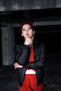 an asian man in a red shirt and black jacket posing with his hands in an abandoned warehouse