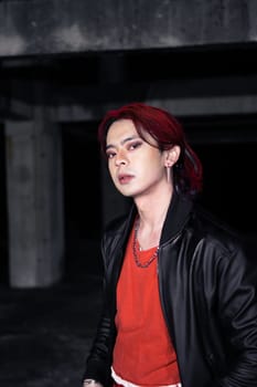 an asian man in a red shirt and black jacket posing with his hands in an abandoned warehouse