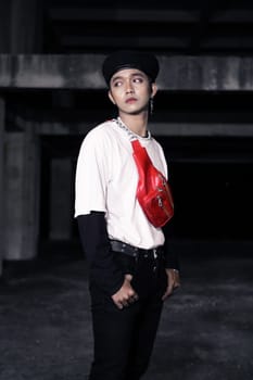 an Asian man with a black cap posing in black pants and a white shirt in a building