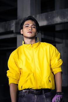 an Asian man with sleek black hair wearing a yellow jacket and jeans while posing in a haunted building