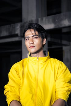 an Asian man with sleek black hair wearing a yellow jacket and jeans while posing in a haunted building