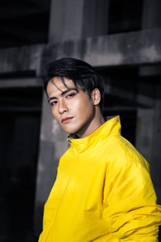 an Asian man with sleek black hair wearing a yellow jacket and jeans while posing in a haunted building