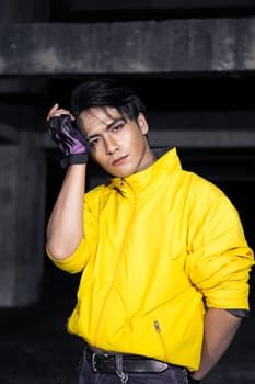 an Asian man with sleek black hair wearing a yellow jacket and jeans while posing in a haunted building