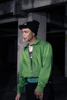 an Asian man smiles while wearing a green parachute jacket and black pants at night