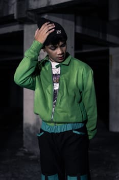 an Asian man smiles while wearing a green parachute jacket and black pants at night