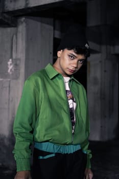 an Asian man smiles while wearing a green parachute jacket and black pants at night