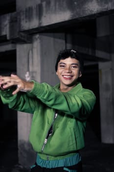 an Asian man smiles while wearing a green parachute jacket and black pants at night