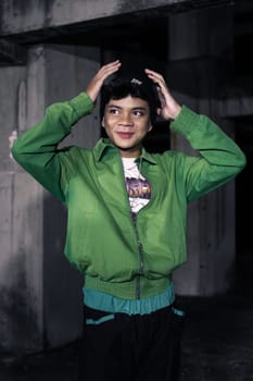 an Asian man smiles while wearing a green parachute jacket and black pants at night