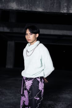 an asian man posing in a white sweater and a chain necklace around his neck in an old building