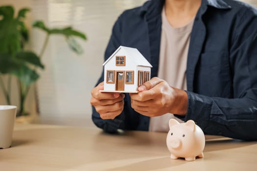 Hands holding a house model and piggy bank, symbolizing mortgage, loan, and property concepts. Highlights financial strategies for saving money, residential tax benefits, and securing a dream home.
