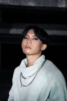 an asian man posing in a white sweater and a chain necklace around his neck in an old building