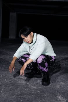 an asian man with black hair squats very masculine in an old building