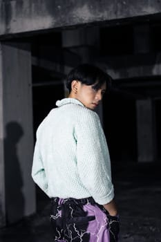 an asian man in black pants with a lightning pattern and a white sweater stands in a haunted building