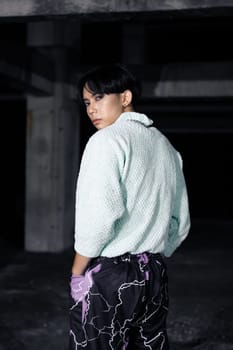 an asian man in black pants with a lightning pattern and a white sweater stands in a haunted building