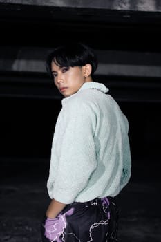 an asian man in black pants with a lightning pattern and a white sweater stands in a haunted building