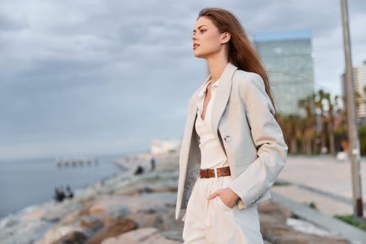 A poised woman in stylish business clothing stands by the waterfront, exuding confidence and professionalism. The serene background enhances the business concept.