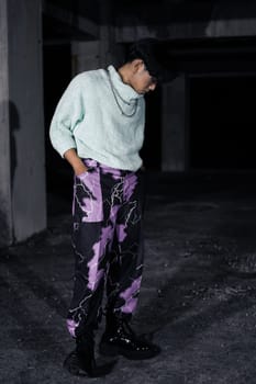 an asian man in black pants with a lightning pattern and a white sweater stands in a haunted building