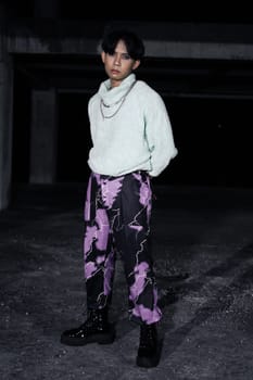 an asian man in black pants with a lightning pattern and a white sweater stands in a haunted building