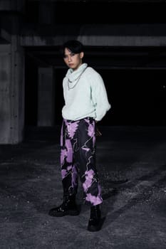 an asian man in black pants with a lightning pattern and a white sweater stands in a haunted building