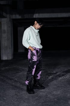 an asian man in black pants with a lightning pattern and a white sweater stands in a haunted building