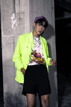 an asian man in a lime colored jacket leaning against a disused building pillar looking very handsome at night