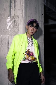 an asian man in a lime colored jacket leaning against a disused building pillar looking very handsome at night
