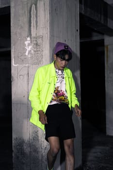an asian man in a lime colored jacket leaning against a disused building pillar looking very handsome at night