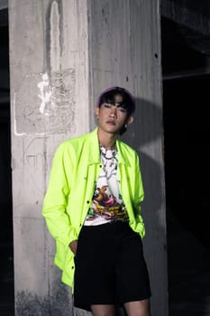 an asian man in a lime colored jacket leaning against a disused building pillar looking very handsome at night