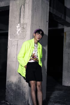 an asian man in a lime colored jacket leaning against a disused building pillar looking very handsome at night