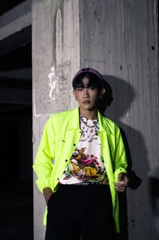 an asian man in a lime colored jacket leaning against a disused building pillar looking very handsome at night