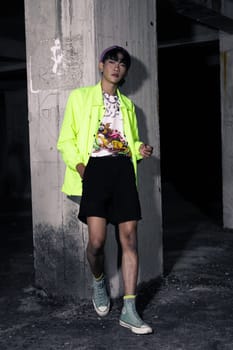 an asian man in a lime colored jacket leaning against a disused building pillar looking very handsome at night